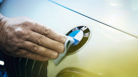 Eine Hand putzt mit einem Tuch das BMW Logo auf der Autohaube Eine Hand putzt mit einem Tuch das BMW Logo auf der Autohaube